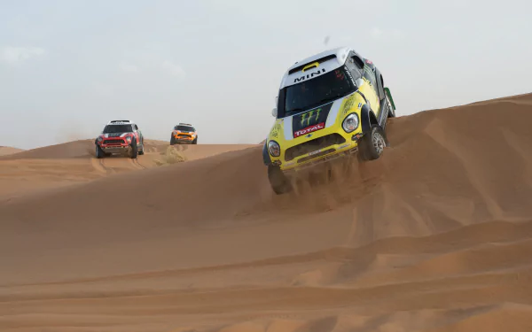 Mini Cooper rally car airborne over desert dunes with two other rally cars in pursuit — 2K Quad HD PC desktop wallpaper/background
