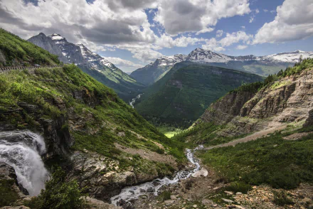 A stunning landscape of Glacier National Park, showcasing a cascading waterfall, winding river, and majestic mountains under a dramatic sky. Perfect for nature lovers.