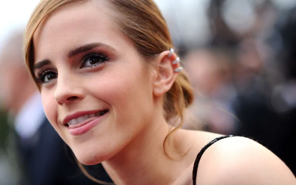 A close-up of Emma Watson smiling at an event, showcasing her stylish look and elegant hairstyle, featuring vibrant details, suitable as a 4K Ultra HD desktop wallpaper and background.