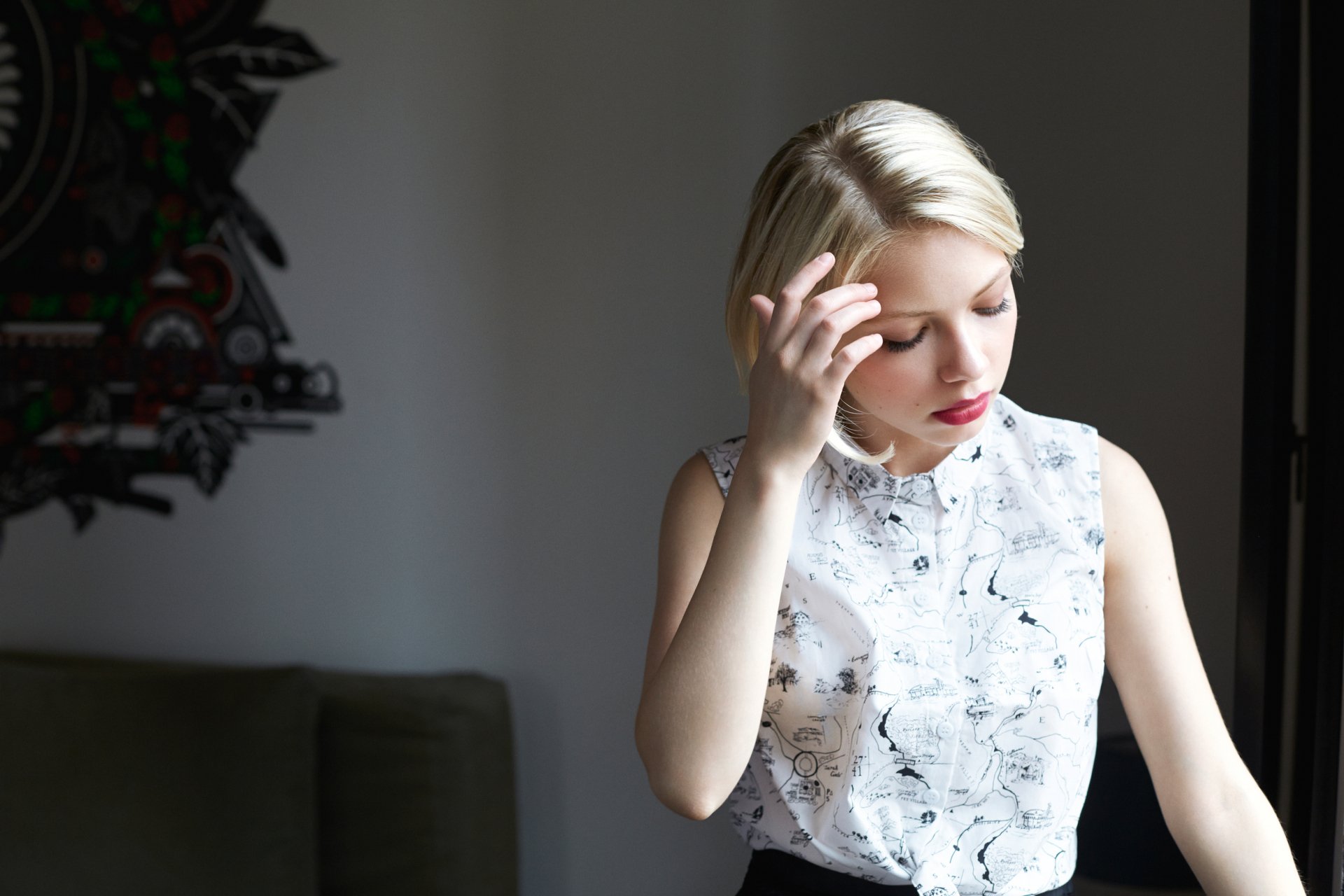 HD PC desktop wallpaper of a blonde American actress: a young woman in a sleeveless floral blouse, red lipstick, touching her hair in a soft indoor portrait.