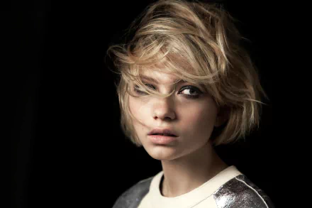 HD desktop wallpaper: close-up portrait of a blonde actress with short tousled hair, striking face and pensive expression against a dark, moody background.