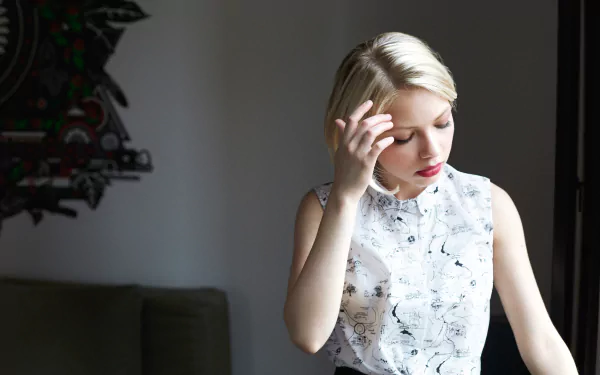HD PC desktop wallpaper of a blonde American actress: a young woman in a sleeveless floral blouse, red lipstick, touching her hair in a soft indoor portrait.