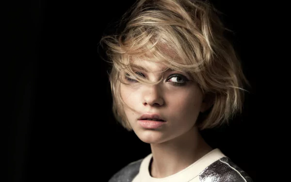 HD desktop wallpaper: close-up portrait of a blonde actress with short tousled hair, striking face and pensive expression against a dark, moody background.
