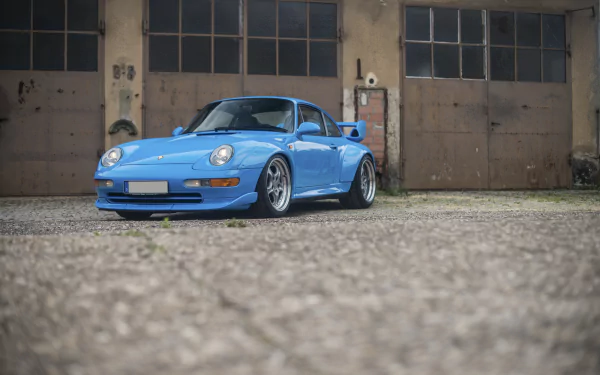 Blue Porsche 911 GT2 parked in front of worn industrial garage doors — Porsche 911 vehicle presented as a 4K Ultra HD PC desktop wallpaper/background.