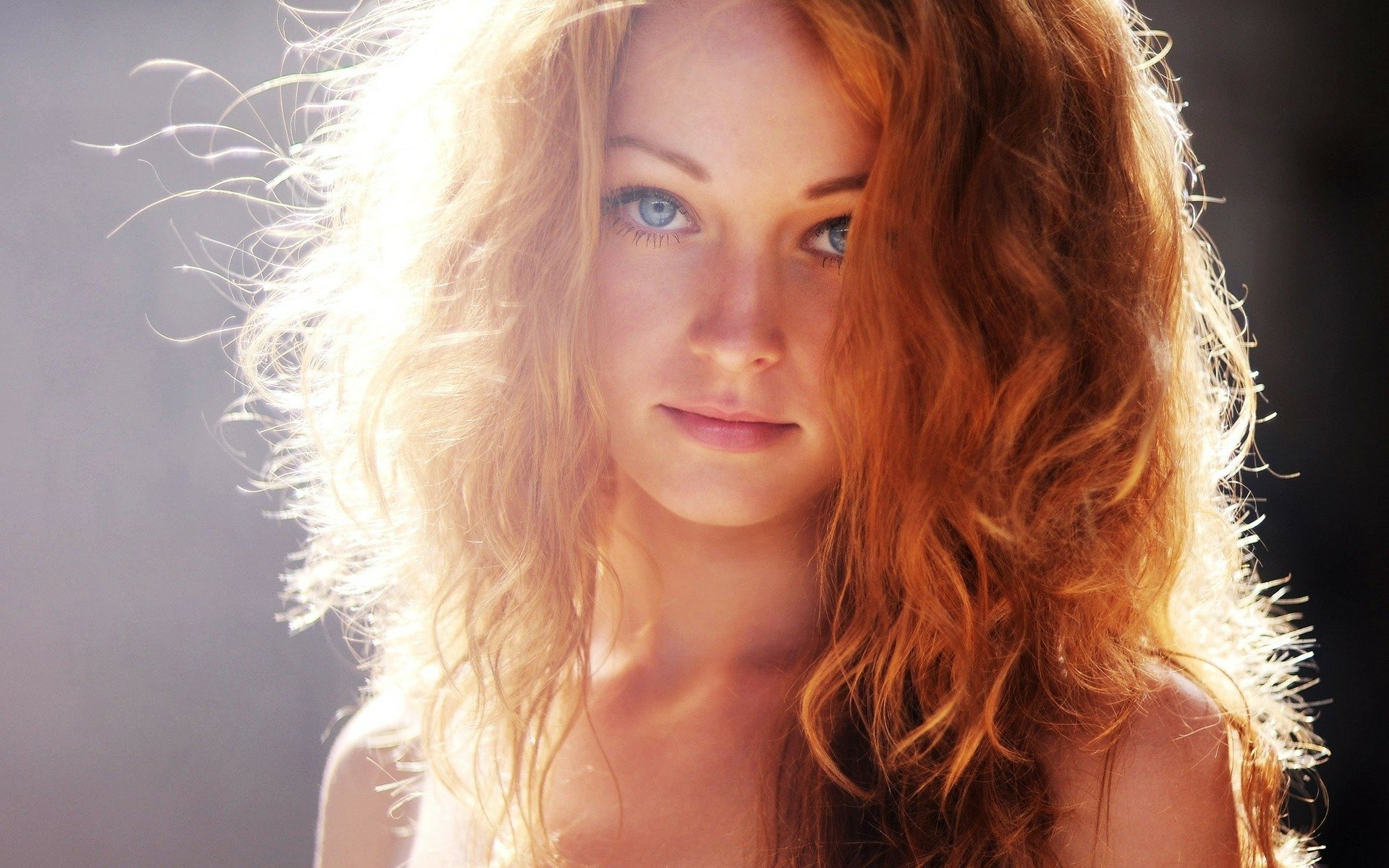 HD desktop wallpaper featuring a model with voluminous, wavy brown hair and a serene expression illuminated by soft, natural light.