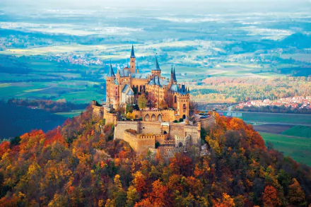 A stunning view of Hohenzollern Castle surrounded by vibrant fall foliage in a picturesque forest landscape, captured in 4K Ultra HD for a striking desktop wallpaper.