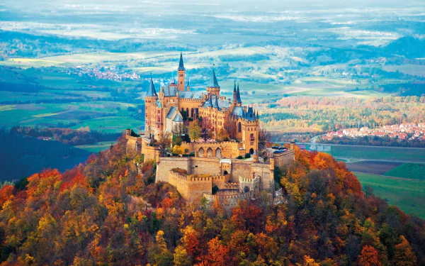 A stunning view of Hohenzollern Castle surrounded by vibrant fall foliage in a picturesque forest landscape, captured in 4K Ultra HD for a striking desktop wallpaper.
