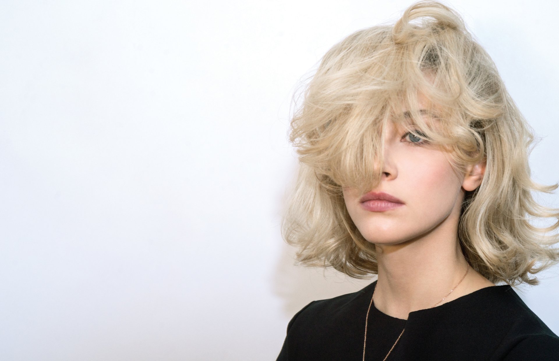 Close-up portrait of Canadian actress Sarah Gadon with blonde hair partially covering her face, set against a plain background.