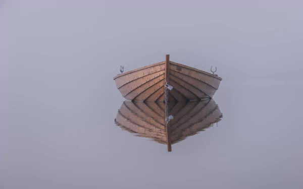 A serene rowboat floats in a fog-covered landscape, perfectly mirrored in calm water, creating a tranquil scene for this 4K Ultra HD desktop wallpaper.