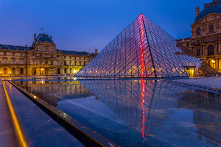 A stunning view of the Louvre at night, showcasing the illuminated glass pyramid reflecting in the surrounding water, highlighting the beauty of Parisian architecture.