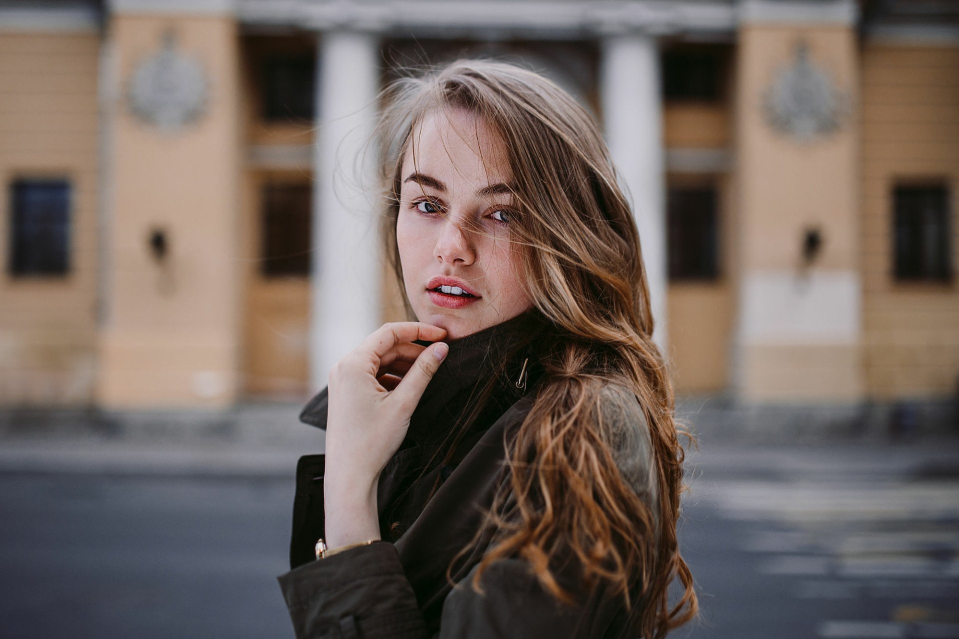 HD desktop wallpaper of a brunette female model with striking blue eyes, posing outdoors against a blurred urban background.