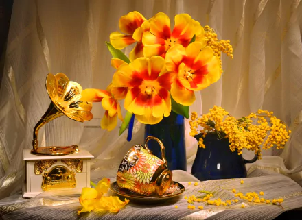 HD desktop wallpaper featuring a still life of vibrant yellow and orange tulips in a vase, a vintage gramophone, and a decorative cup arranged on a draped fabric background.
