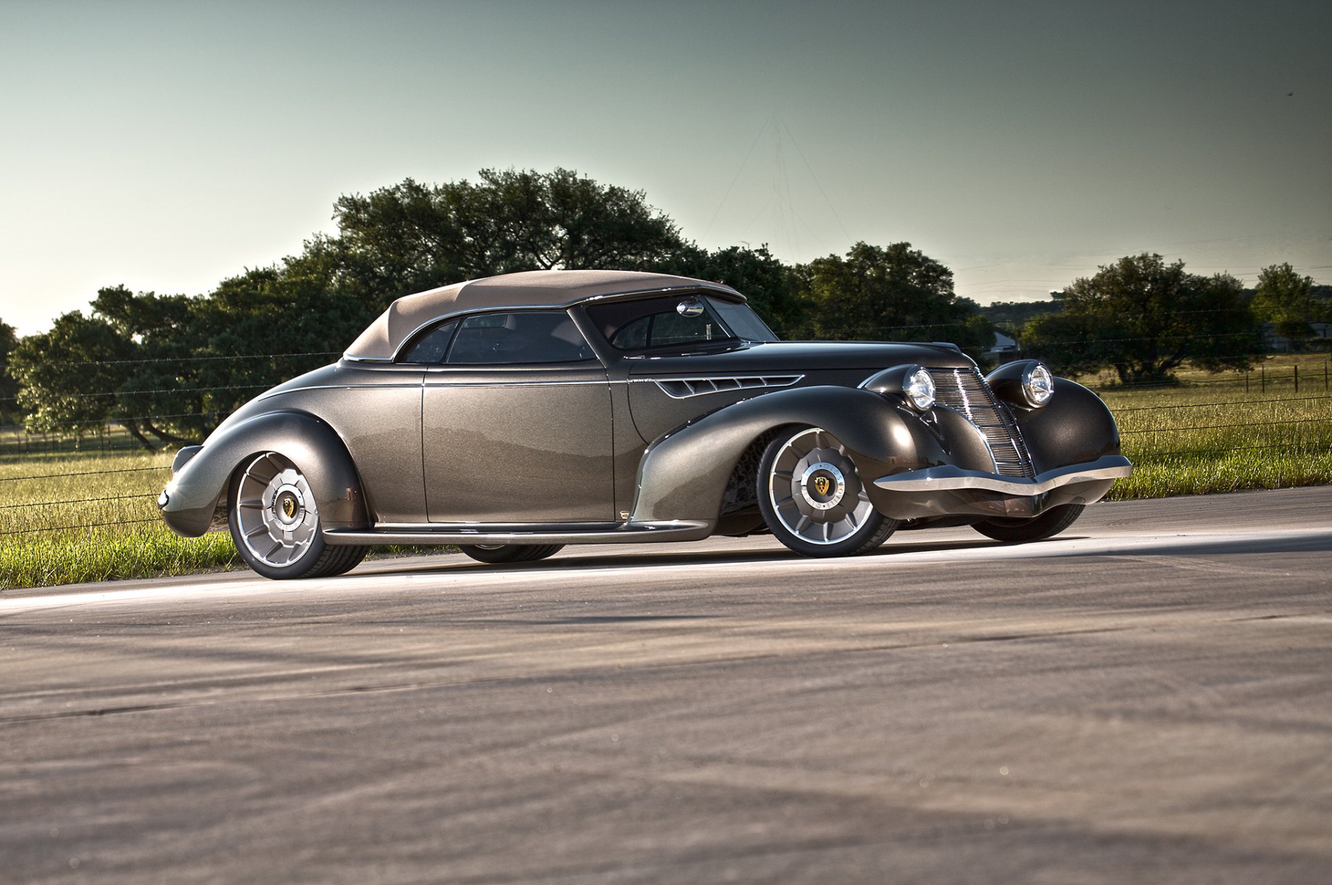 A sleek, vintage 1939 Oldsmobile hot rod parked on a paved road with green fields and trees under a clear sky, captured in high-definition for a PC desktop background.