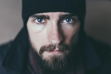 Close-up portrait of a bearded man with piercing blue eyes wearing a dark beanie; 5K Ultra HD PC desktop wallpaper and background.
