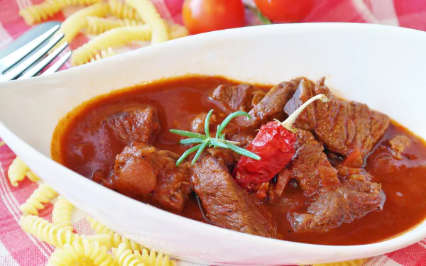 4K Ultra HD wallpaper featuring a close-up of richly spiced meat stew garnished with herbs, served alongside pasta on a vibrant, colorful background.