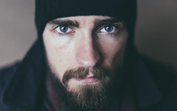 Close-up portrait of a bearded man with piercing blue eyes wearing a dark beanie; 5K Ultra HD PC desktop wallpaper and background.
