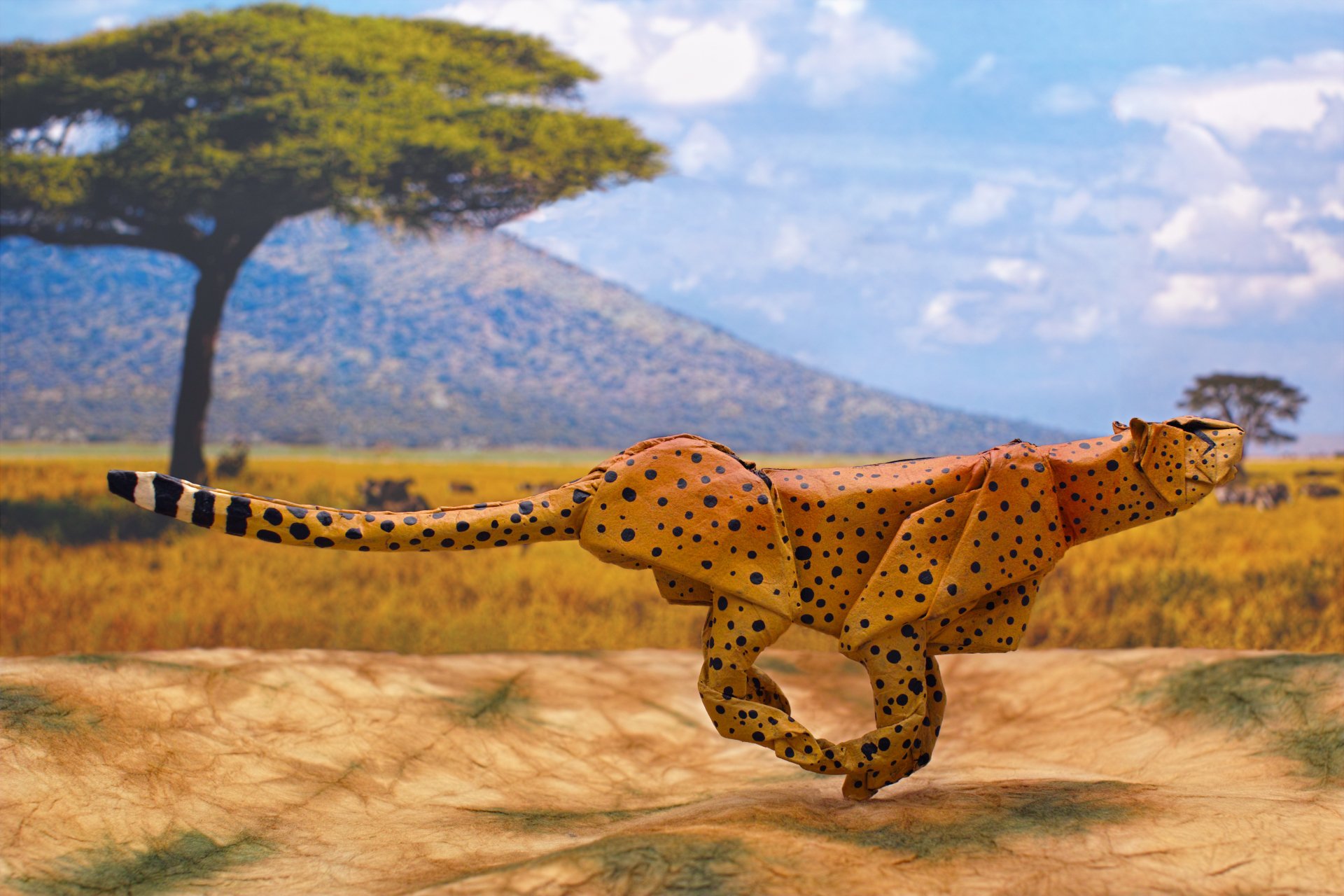 A man-made origami cheetah runs across a savanna landscape, rendered in 4K Ultra HD as a vibrant PC desktop wallpaper.
