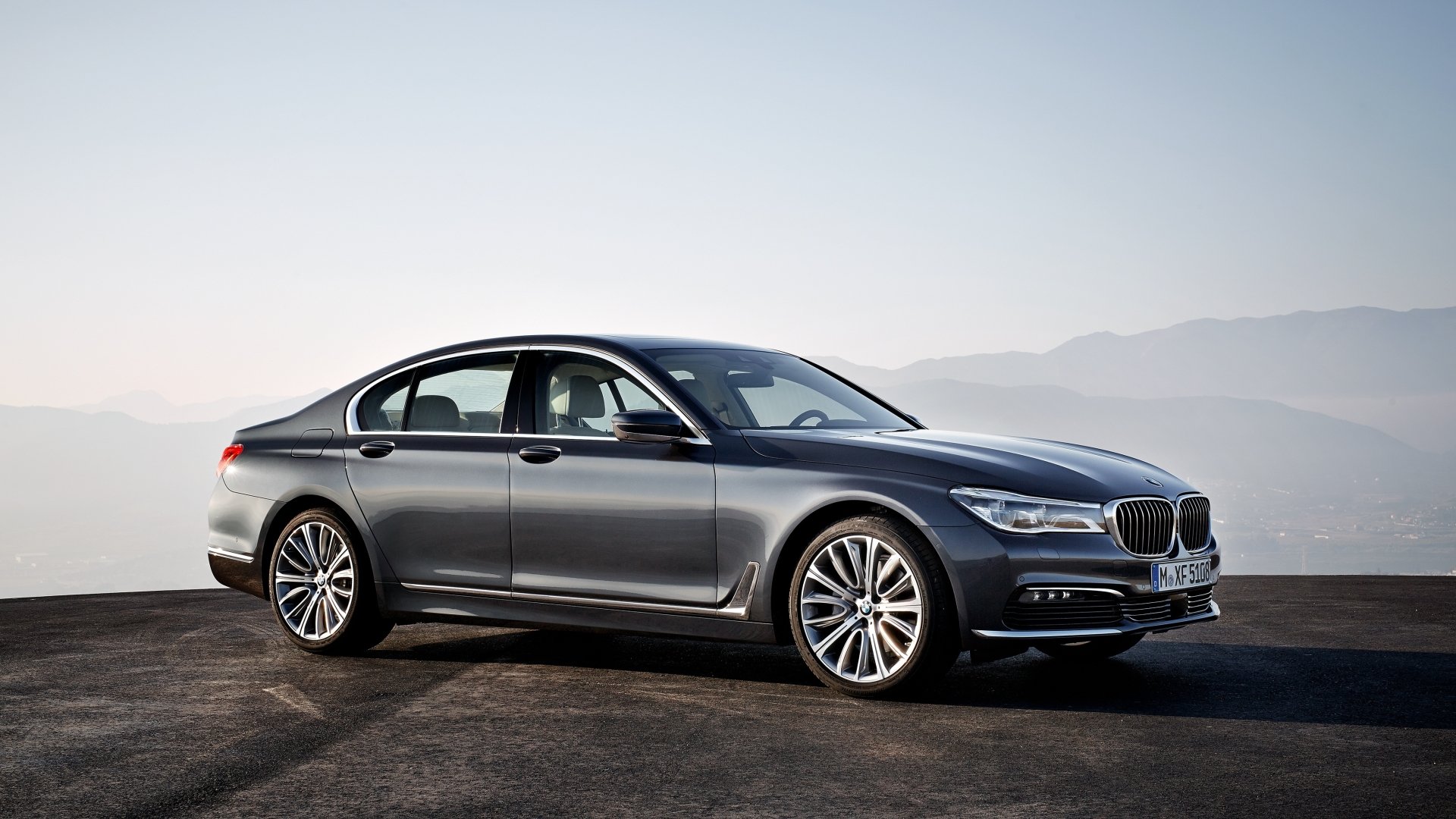 Silver BMW 7 Series sedan displayed on a scenic mountain backdrop in a crisp 4K Ultra HD desktop wallpaper.
