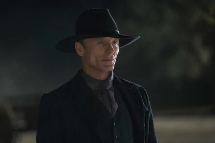 Ed Harris stands in a dark, atmospheric setting from the TV show Westworld, dressed in a black hat and suit, creating a striking HD desktop wallpaper.