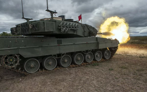 HD desktop wallpaper of a Leopard 2 military tank firing, set against a cloudy sky on rugged terrain.