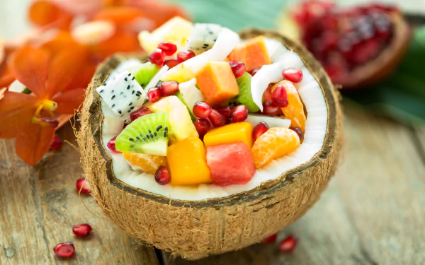 A vibrant 4K Ultra HD desktop wallpaper featuring a fresh coconut shell filled with colorful tropical fruits, including kiwi, dragon fruit, mango, and pomegranate seeds.