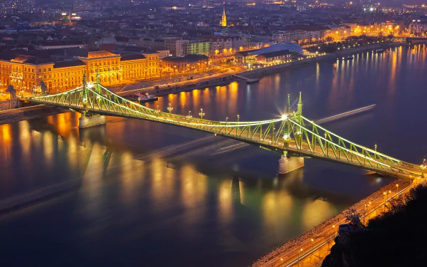 Night view of a brightly lit man-made bridge spanning the Danube River in Budapest, Hungary, with city lights reflecting on the water.