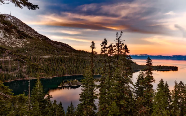 HD landscape wallpaper showing a serene view of Lake Tahoe with a forested island, tall trees, and mountains under a colorful sunset sky.