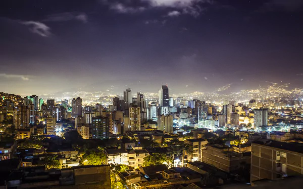A stunning night view of Medellín, Colombia, showcasing its vibrant cityscape filled with towering buildings and shimmering lights against a dark sky. Ideal for a desktop wallpaper.