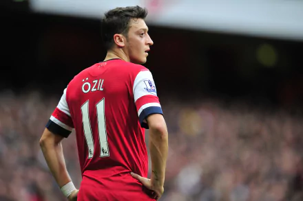 4K Ultra HD image of German soccer player Mesut Özil in action, wearing a red jersey with number 11, set against a blurred stadium background.