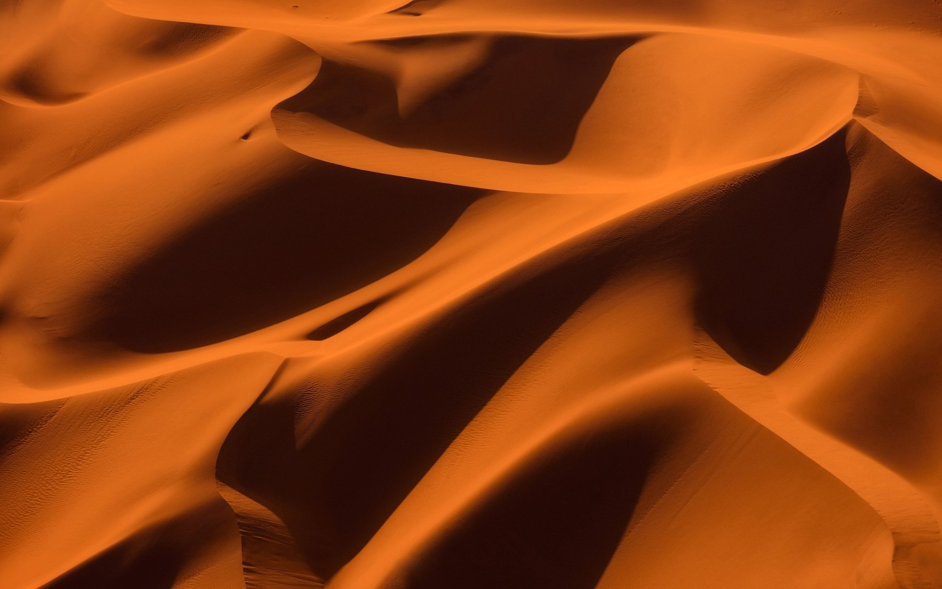 HD nature desktop wallpaper: close-up of rippled desert sand dunes in warm orange light, flowing ridges and deep shadows.