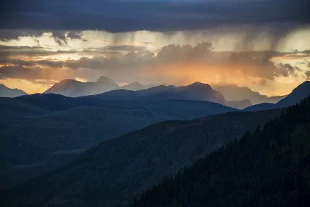 A stunning Montana sunset illuminates the clouds over the mountains, showcasing the dramatic landscape of Glacier National Park in a breathtaking wilderness scene.