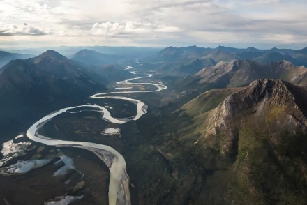 A stunning aerial view of Alaska's wilderness, showcasing a winding river surrounded by majestic mountains and lush landscapes, capturing the essence of nature's beauty.