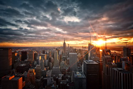 Aerial view of New York City skyline at dawn with sunbeams breaking through clouds over skyscrapers on the horizon, showcasing a vibrant urban cityscape.
