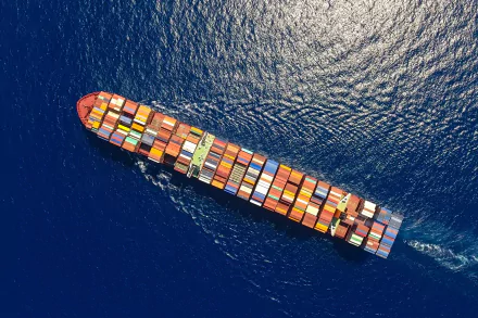 Aerial view of a large container ship navigating through deep blue ocean waters, showcasing vibrant cargo containers against the serene backdrop, perfect for HD desktop wallpaper.