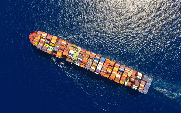 Aerial view of a container ship loaded with colorful cargo containers sailing across the deep blue ocean, captured in high-definition for a PC desktop wallpaper.