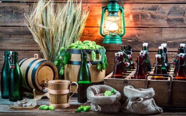 A 4K Ultra HD still life of beer bottles, a wooden barrel, wheat stalks, hop cones, burlap sacks, and a glowing lantern arranged on a rustic wooden surface.