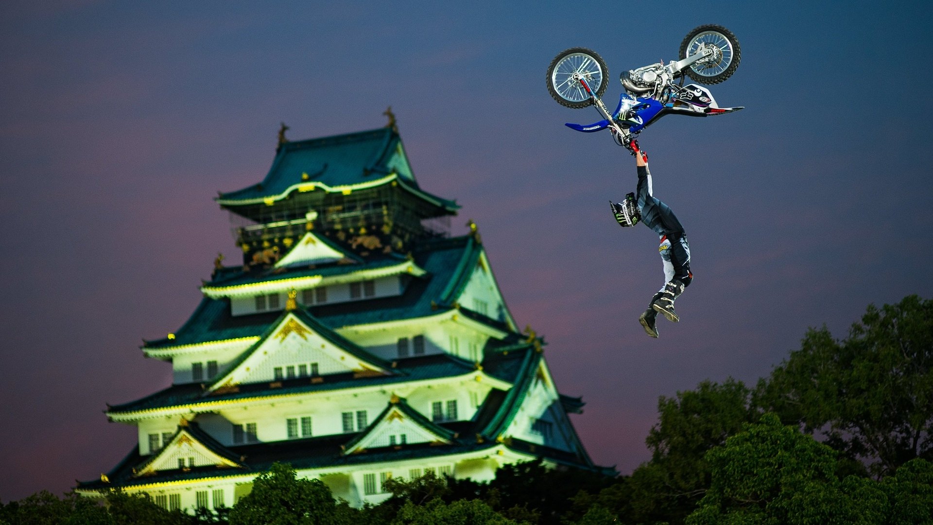 HD desktop wallpaper of a motocross rider performing a high-flying stunt against a twilight sky with a traditional Japanese castle in the background, showcasing sport and skill.