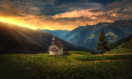 Sunset over a mountain landscape with a small chapel nestled among trees and forest, creating a peaceful and scenic HD desktop wallpaper background.