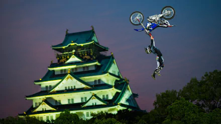 HD desktop wallpaper of a motocross rider performing a high-flying stunt against a twilight sky with a traditional Japanese castle in the background, showcasing sport and skill.