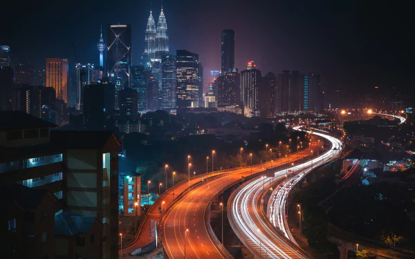 A stunning night view of Kuala Lumpur featuring the illuminated Petronas Towers and a bustling highway with light trails, showcasing the vibrant cityscape of Malaysia.