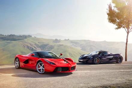 HD wallpaper featuring a red Ferrari LaFerrari and a purple McLaren P1 supercar parked on a scenic hillside road under a clear sky.