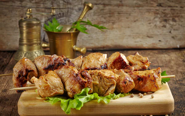 Close-up of grilled meat skewers on a wooden board with lettuce, styled as a 4K Ultra HD still life barbecue food desktop wallpaper background.