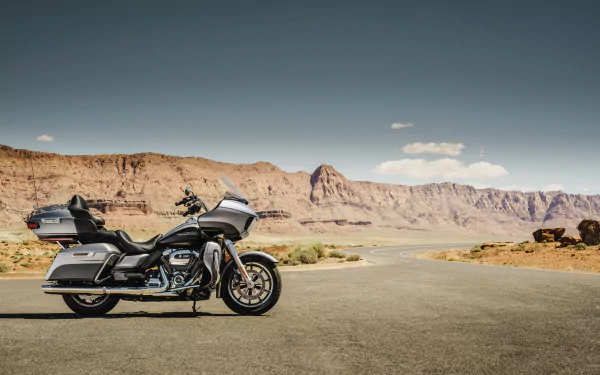 A Harley-Davidson Road Glide Ultra motorcycle parked on an open desert road with rocky cliffs in the background, featured as an HD PC desktop wallpaper.