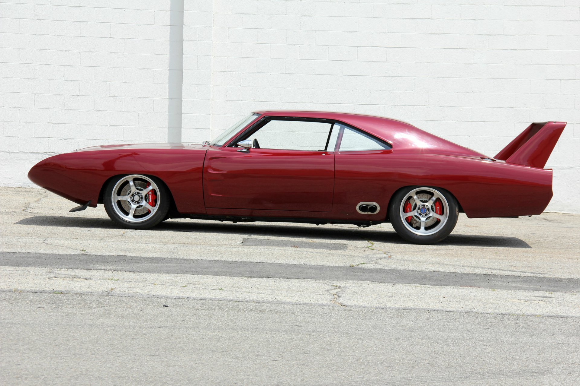 Red custom hot rod coupe with rear wing, side view, parked by a white brick wall. 2K Quad HD PC desktop wallpaper and background.