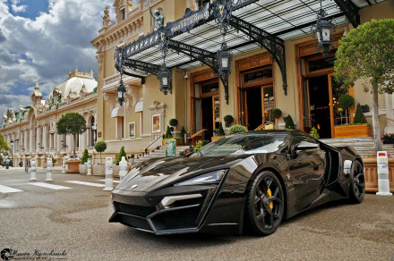 HD PC desktop wallpaper featuring a sleek black Lykan HyperSport parked in front of an ornate, historic building under a partly cloudy sky.