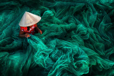 HD PC desktop wallpaper photograph from Phan Rang: a person in a conical hat arranging emerald fishing nets, flowing textures filling the frame.