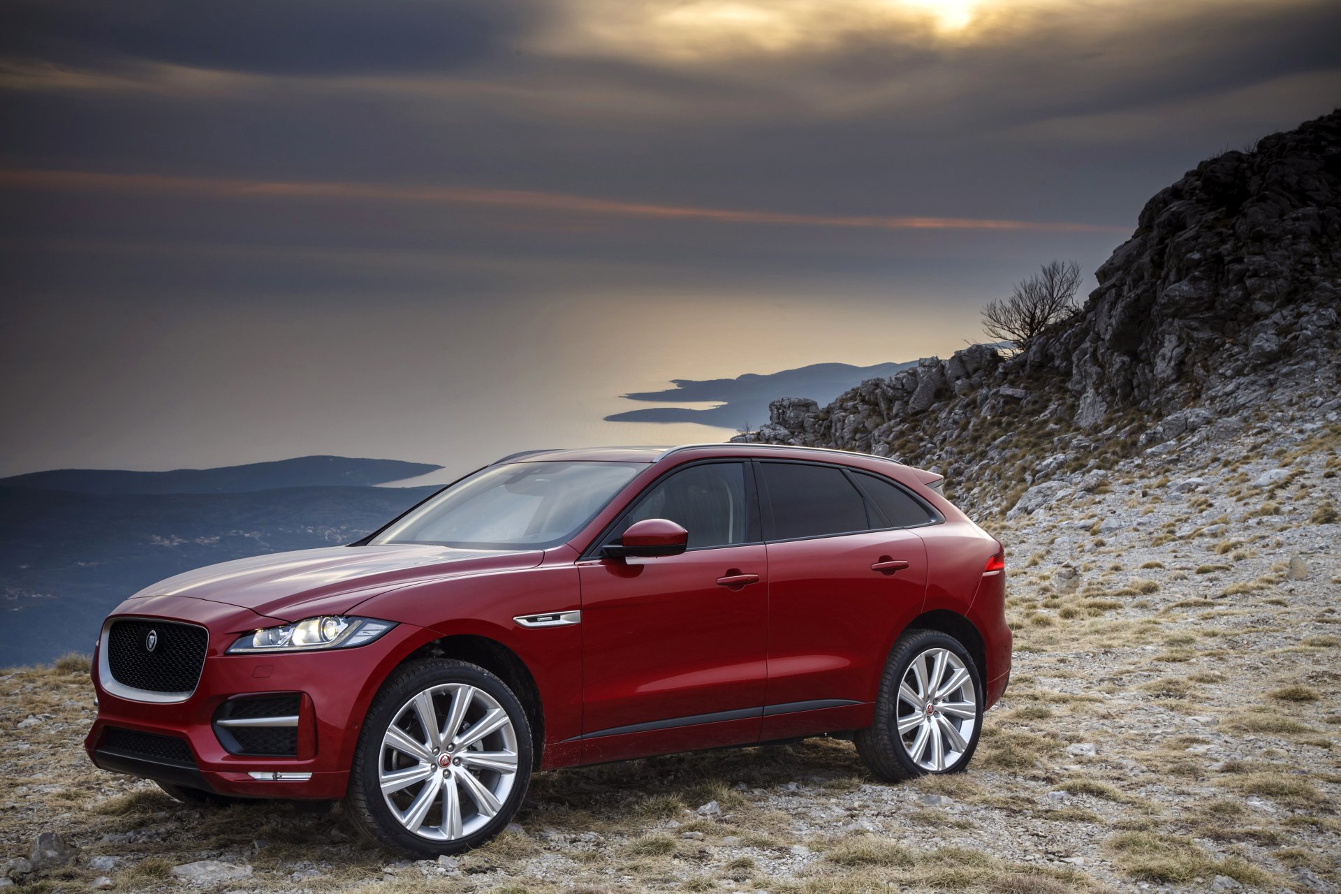 A red Jaguar F-PACE SUV parked on rocky terrain with a scenic coastal background, captured in 4K Ultra HD as a PC desktop wallpaper.