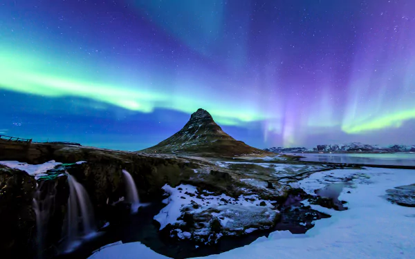 Aurora borealis illuminates the winter sky over Kirkjufell, a snowy mountain near the Kirkjufoss waterfall in Iceland’s stunning natural landscape.