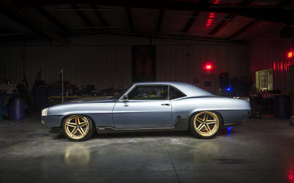 Silver Chevrolet Camaro muscle car hot rod with gold wheels parked in a dim garage, studio lighting — HD PC desktop wallpaper background.