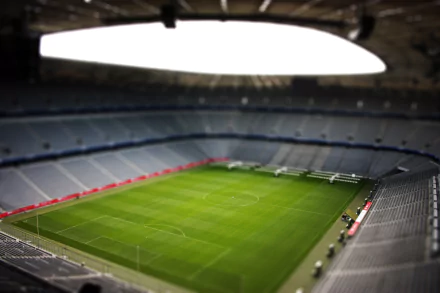 A tilt-shift aerial view of a Munich soccer stadium, captured in vibrant 4K Ultra HD, highlighting the green pitch and surrounding empty stands.